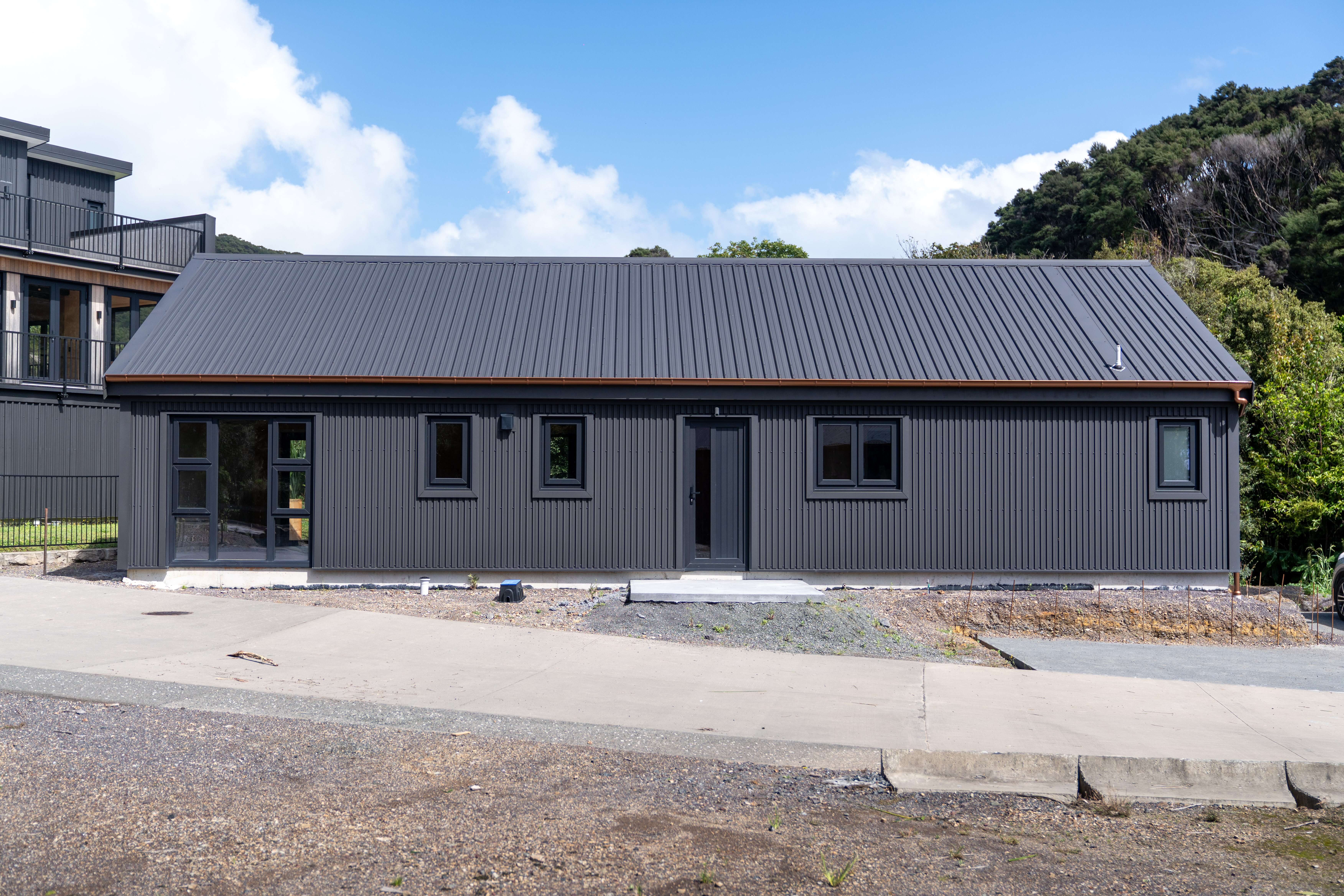 The Tāne — a two-storey solid timber family home with a tall gabled glass wall and wraparound deck