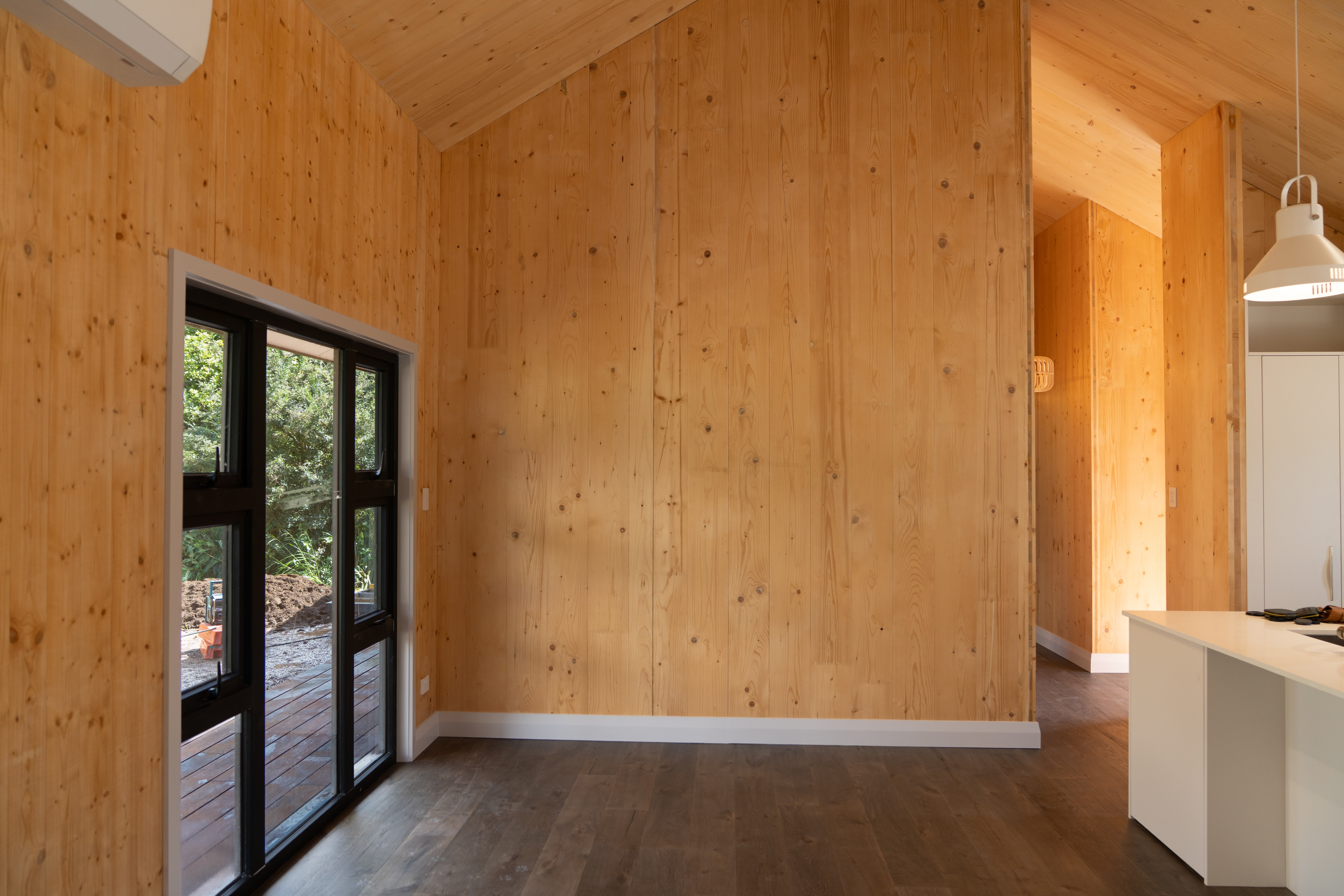 Single-storey solid timber home with long deck on rural New Zealand pasture